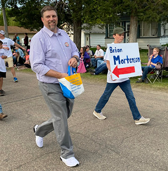 Brian Mortenson handing out candy in the parade with a young man holding a sign with his name on it